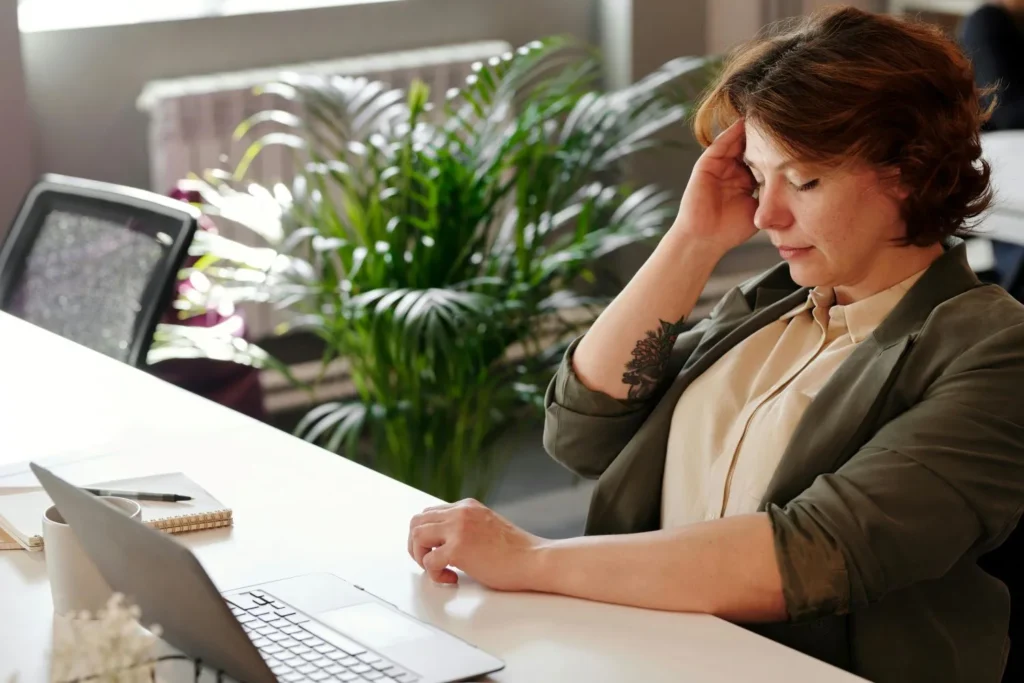 Témoignage après un burn out : une femme qui se tient la tête devant son ordinateur et son carnet